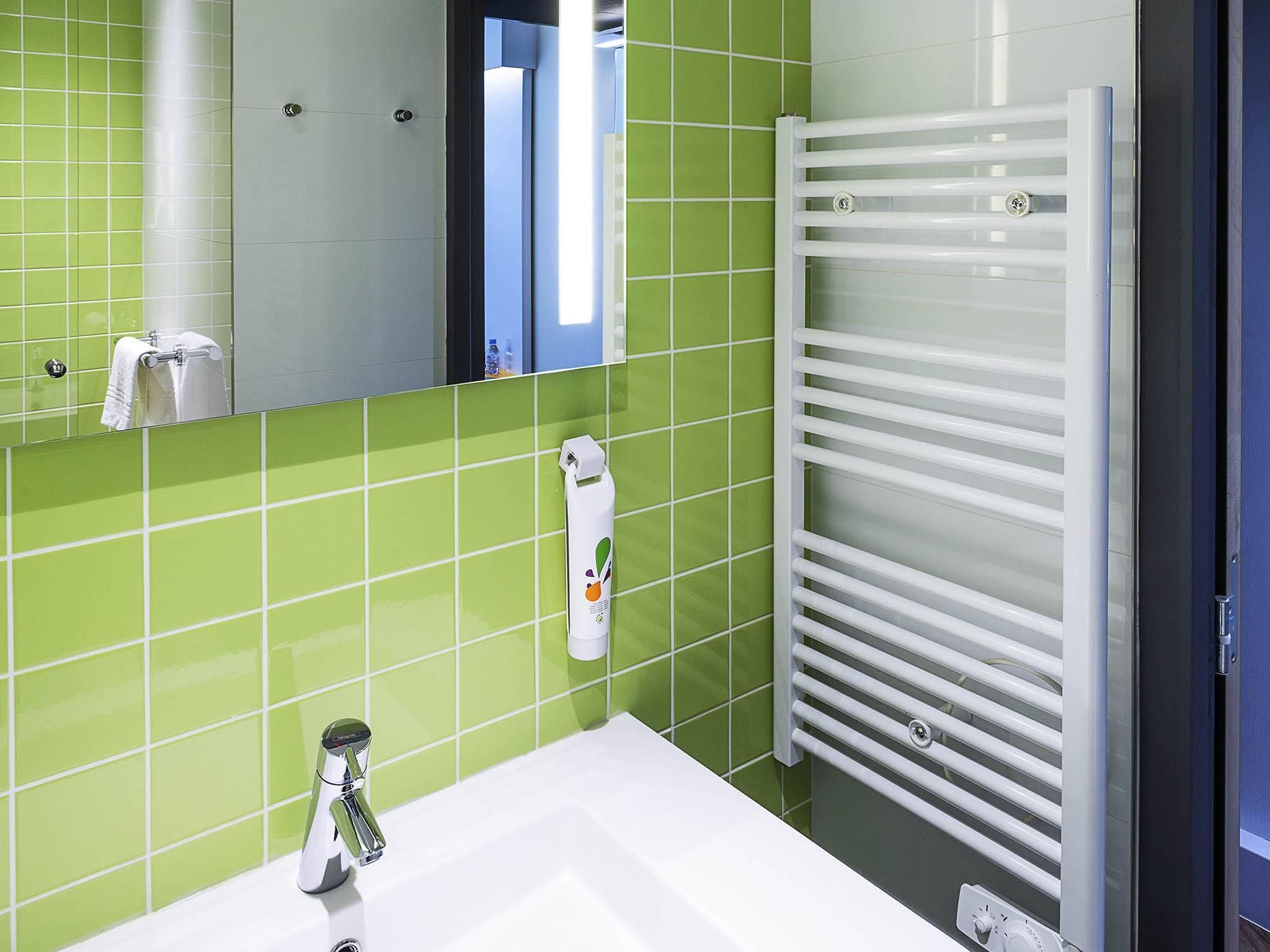 A bathroom with green tiles, a white sink, a mirror, and a towel rack.