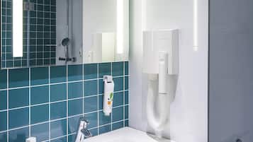 A modern bathroom with a white sink, a handheld showerhead, a towel dispenser, and a mirror.