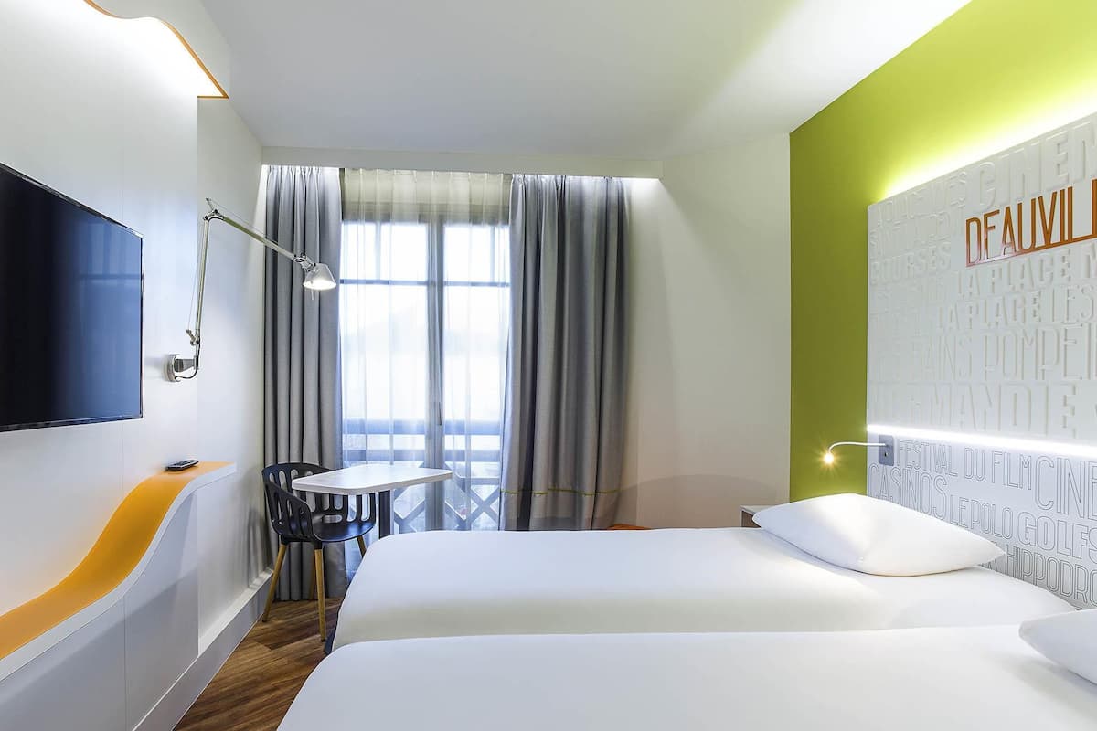 Une chambre dâhĂŽtel avec un lit, un bureau et une chaise, une tĂ©lĂ©vision et une fenĂȘtre avec des rideaux.
