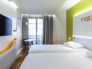 Hotellihuone, jossa on sänky, työpöytä tuolilla, televisio ja ikkuna, jossa on verhot.