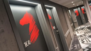 A hotel corridor with mirrored walls, a geometric patterned floor, and a red logo on the doors. - ibis Styles Deauville Centre (Deauville)