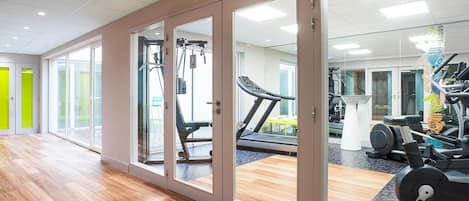 Ein Fitnessraum mit Trainingsgeräten, Laufband und einer Spiegelwand.