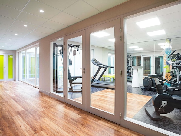 Un gimnasio con equipo de ejercicio, una cinta de correr y un espejo grande.