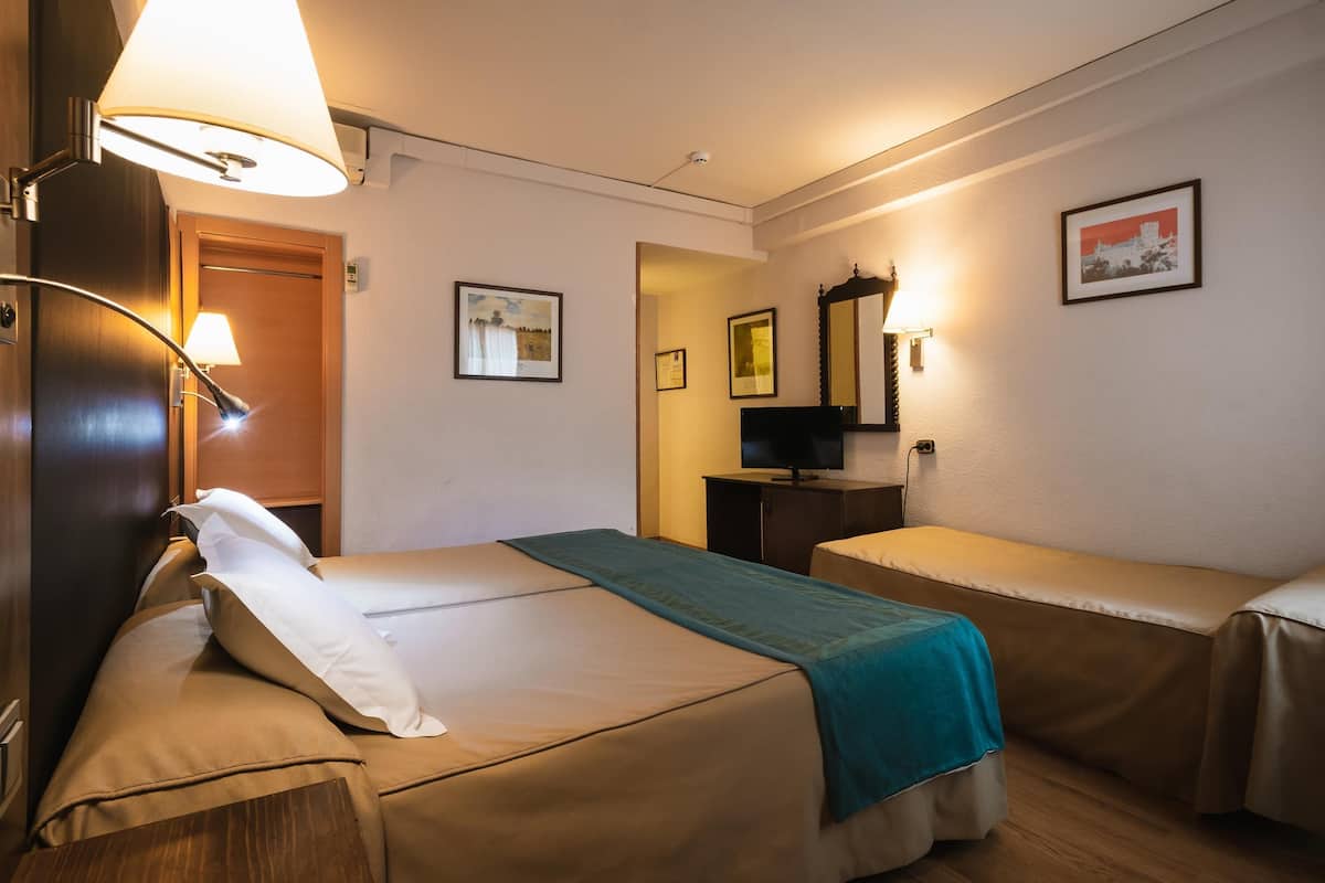 Habitación de hotel con dos camas, televisión, espejo y cuadros en la pared.