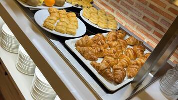 Un bufé con diversas opciones de comida, incluyendo frutas, pasteles y pan.