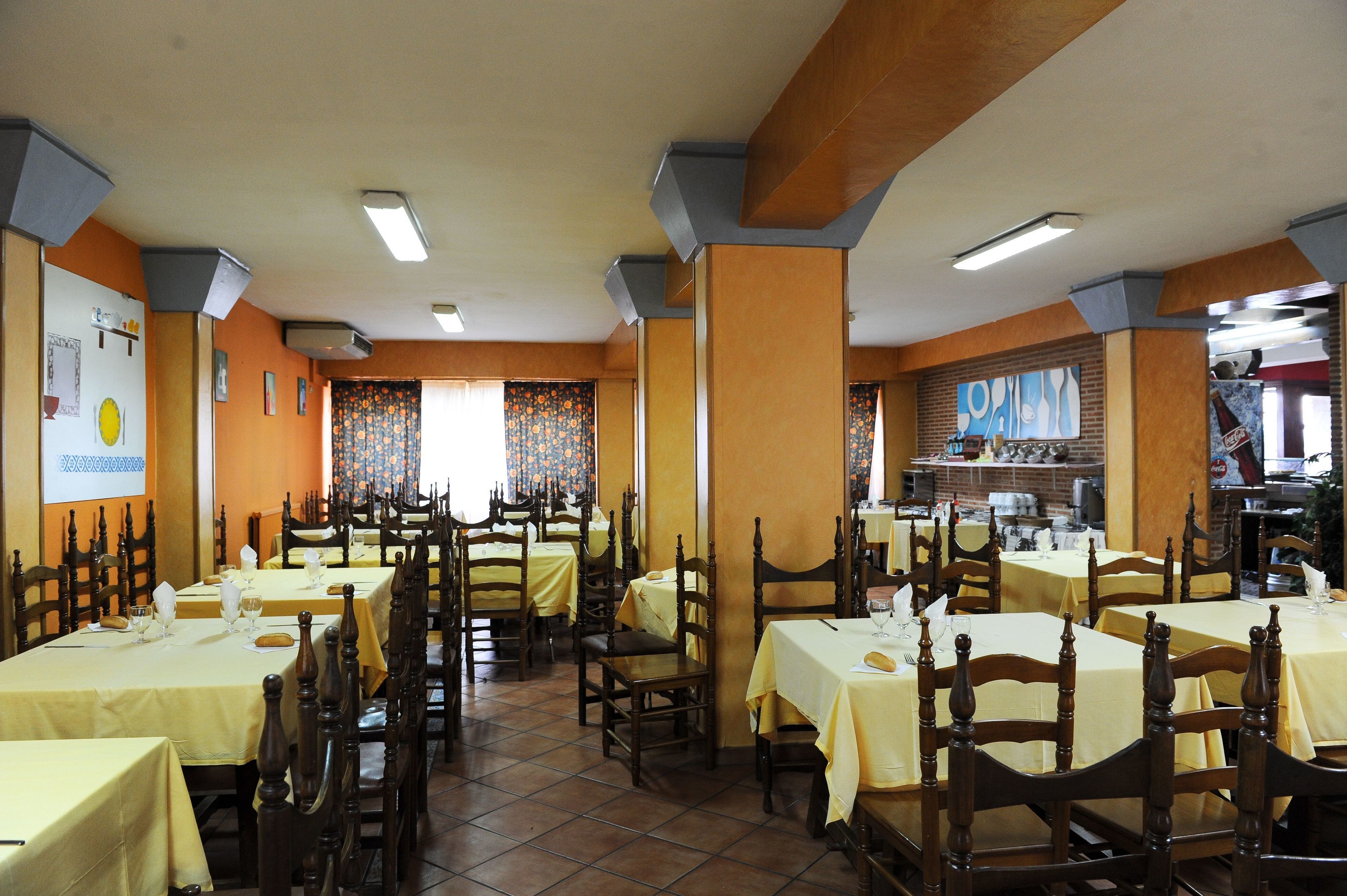 A restaurant with multiple tables and chairs, arranged in a spacious layout with a tiled floor and wooden chairs.