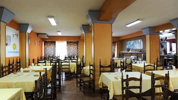 A restaurant with multiple tables and chairs, arranged in a spacious layout with a tiled floor and wooden chairs.