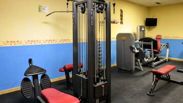 Een sportschool met diverse trainingsapparaten, waaronder een kabeltrekmachine, bankjes en een gewichtstoestel.