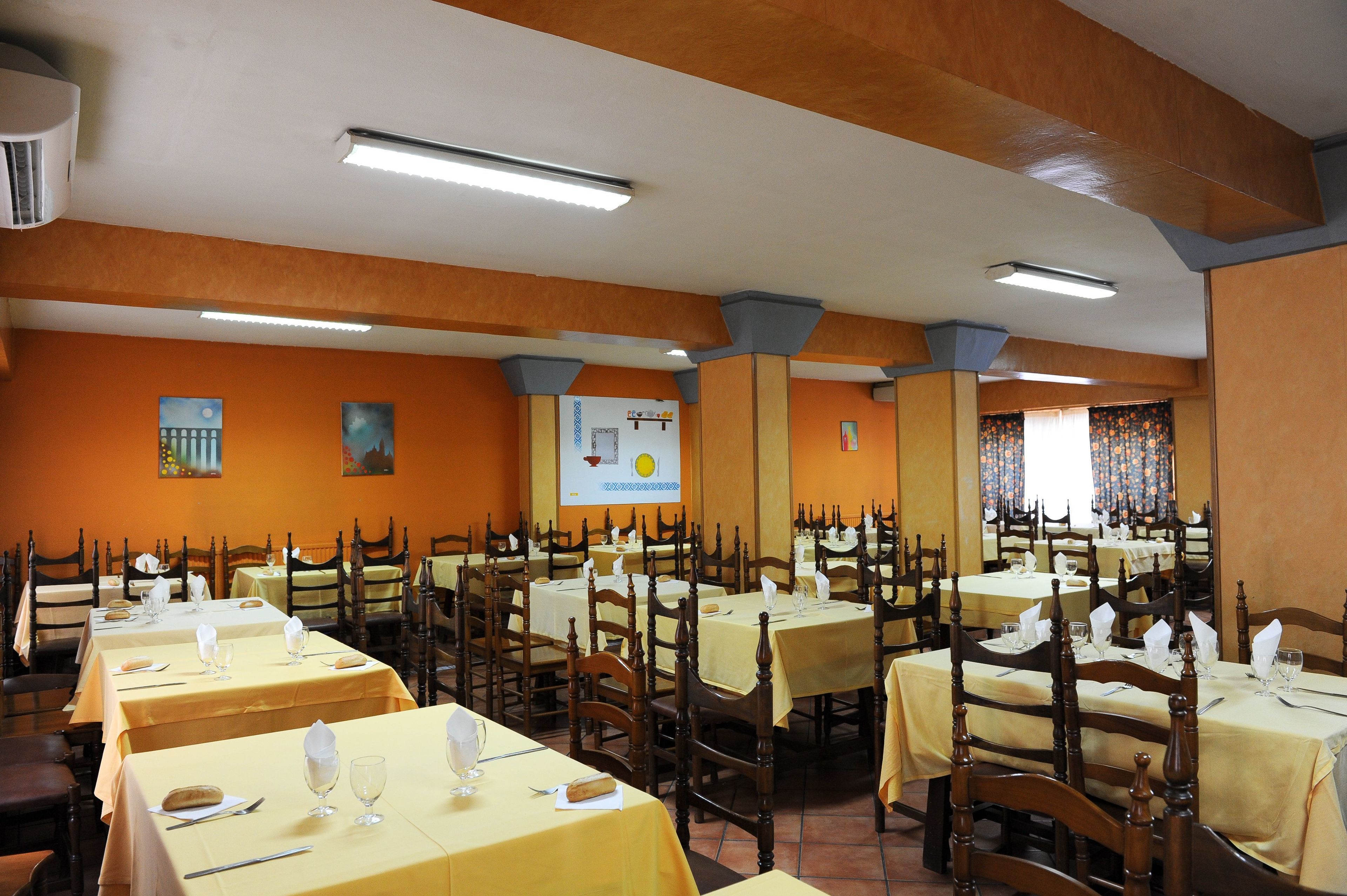 Un espace repas avec plusieurs tables dressées, des chaises en bois et un écran de projection fixé au mur.
