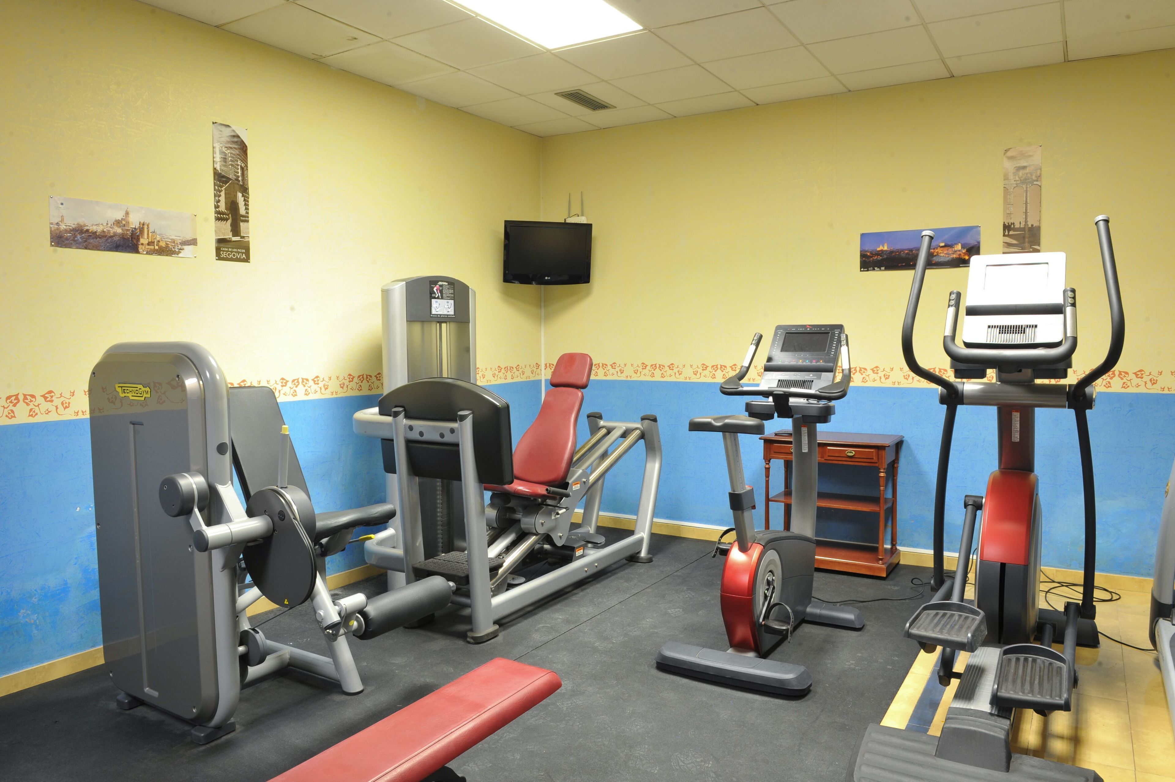 Een sportschool met diverse fitnessapparaten, waaronder een loopband, een crosstrainer en gewichtstoestellen.