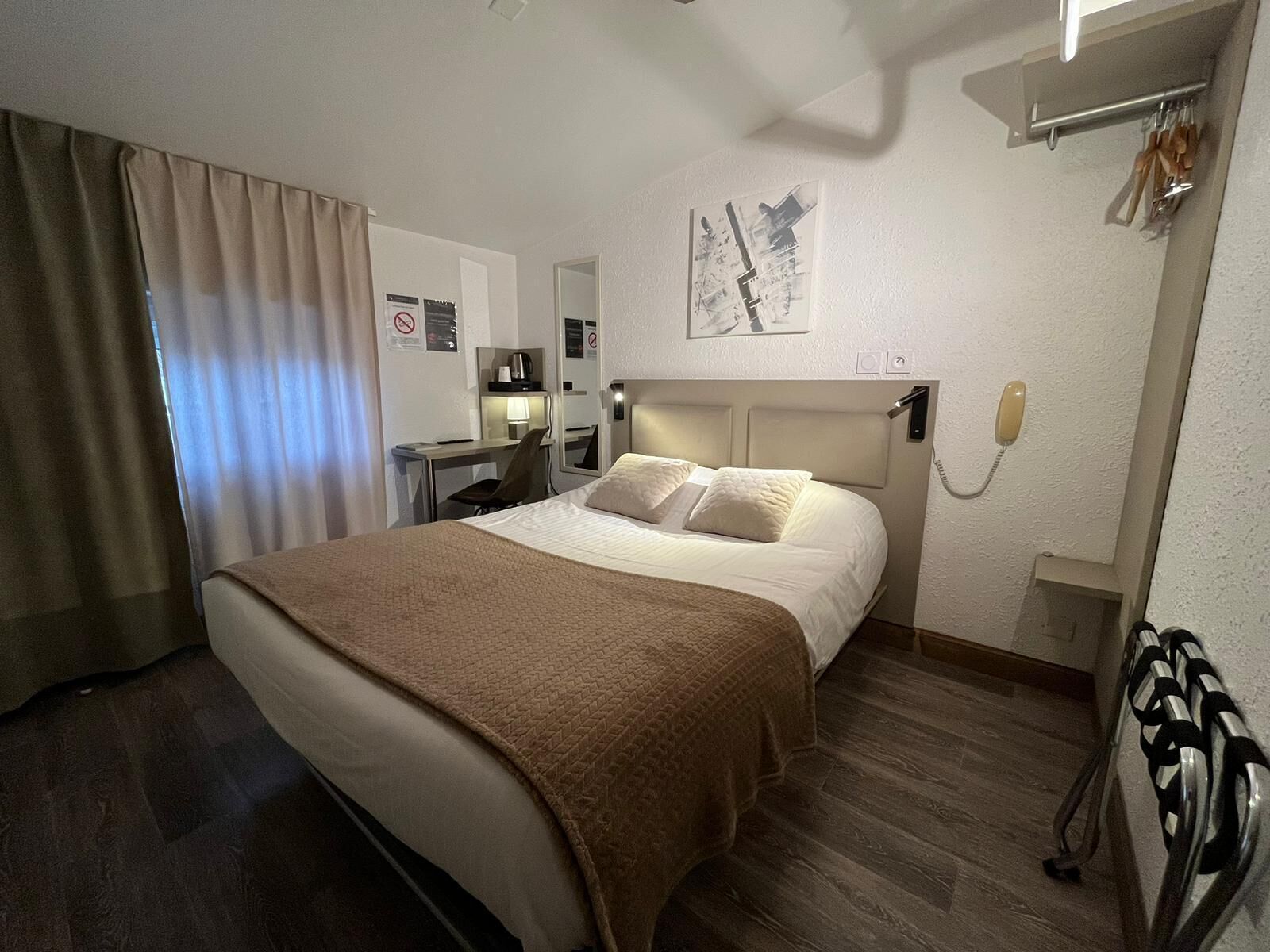 Habitación de hotel con cama, escritorio, silla, teléfono y un cuadro en la pared.