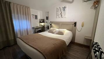Habitación de hotel con cama, escritorio, silla, teléfono y un cuadro en la pared.
