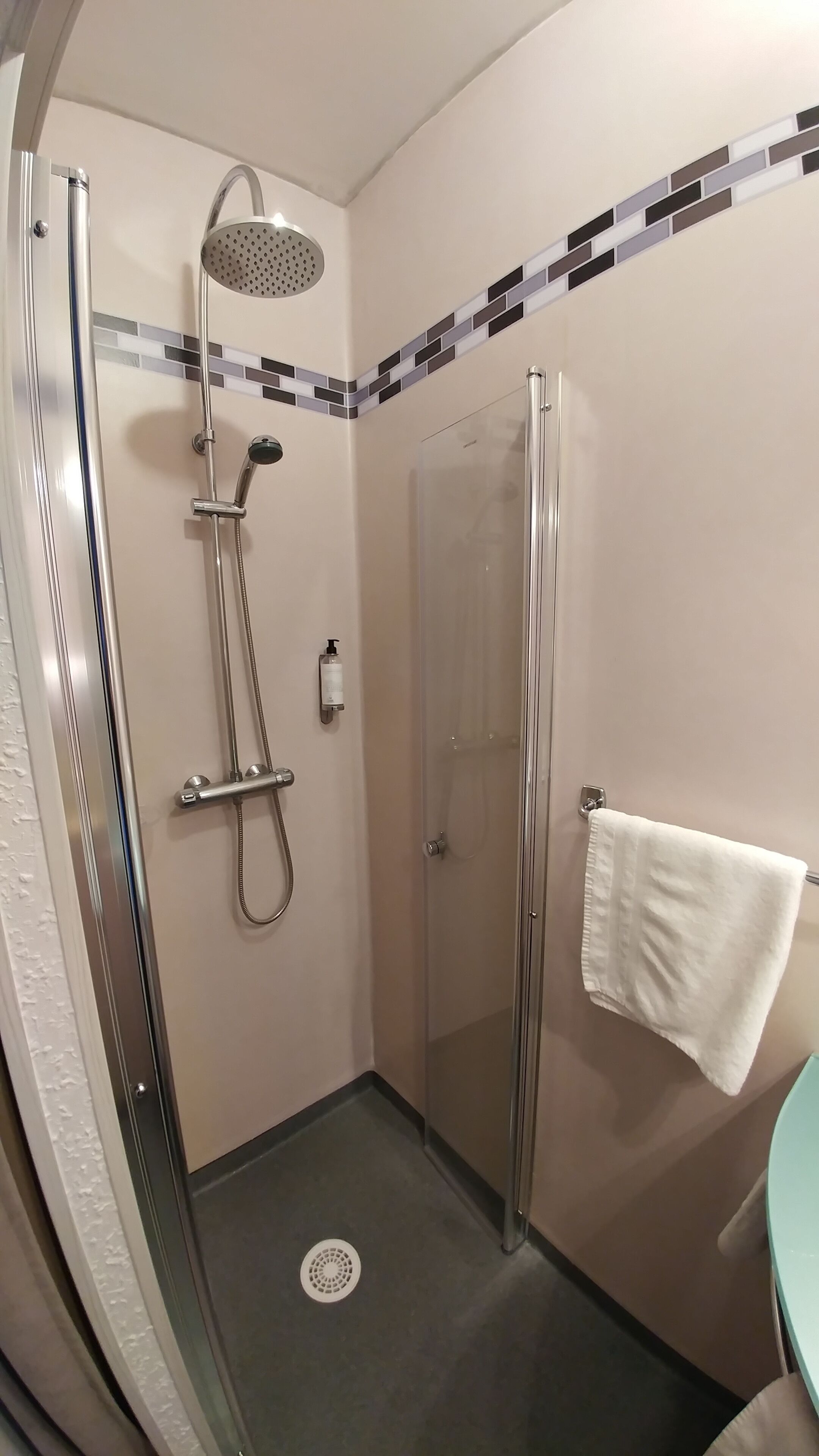 Un baño moderno con ducha envuelta en vidrio, cabezal de ducha manual y toallero con una toalla blanca.