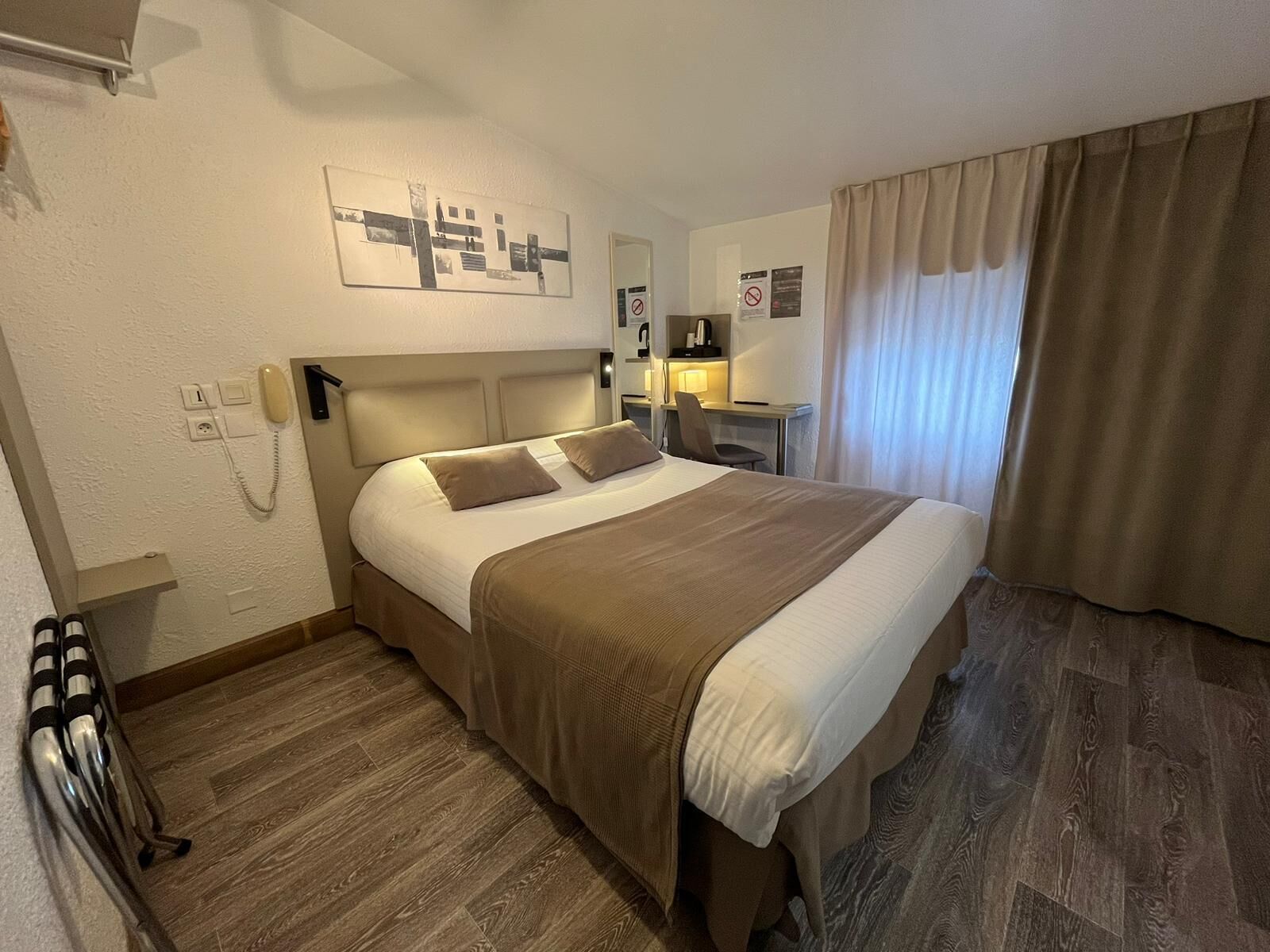 Une chambre d’hôtel équipée d’un lit, d’un bureau, d’une chaise, d’un téléphone et d’une fenêtre avec des rideaux.