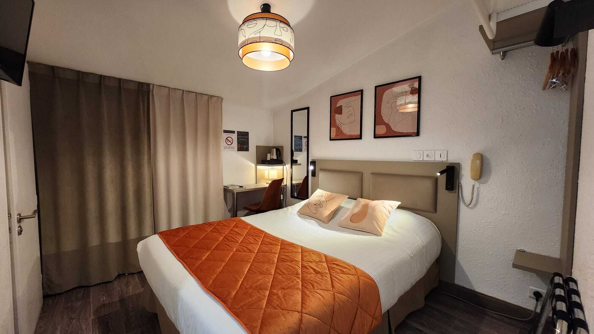A hotel room with a bed, a desk, a chair, a nightstand, a lamp, and a telephone.