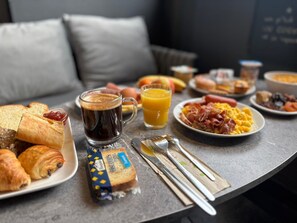 A breakfast table with croissants, a coffee mug, a juice glass, and various breakfast items. - Hôtel Le Cheval Blanc, Cognac Centre (Cognac)