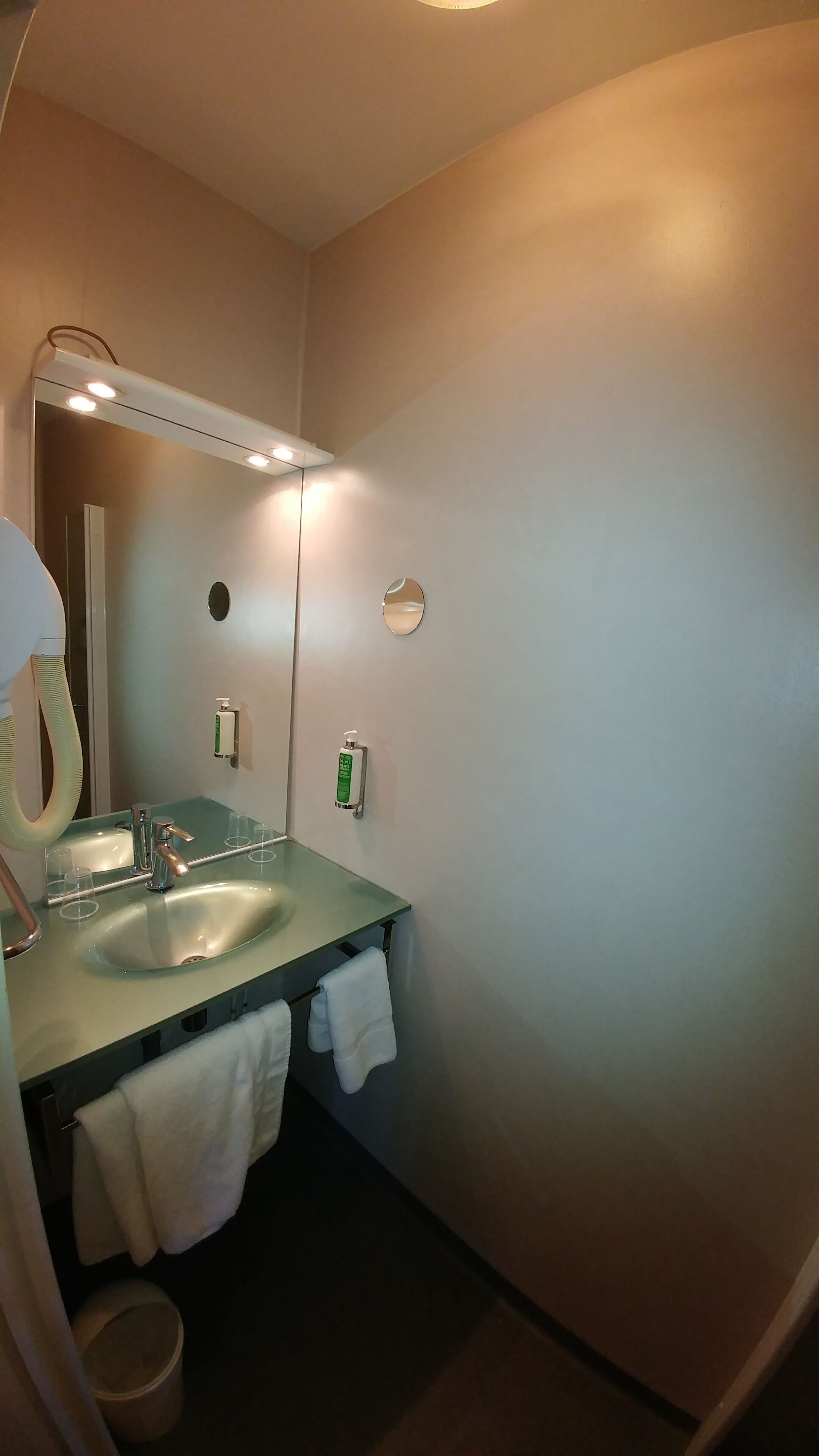 Een badkamer met een wastafel, spiegel en twee handdesinfecterende dispensers.