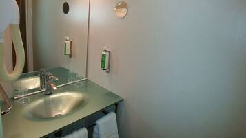 Een badkamer met een wastafel, spiegel en twee handdesinfecterende dispensers.