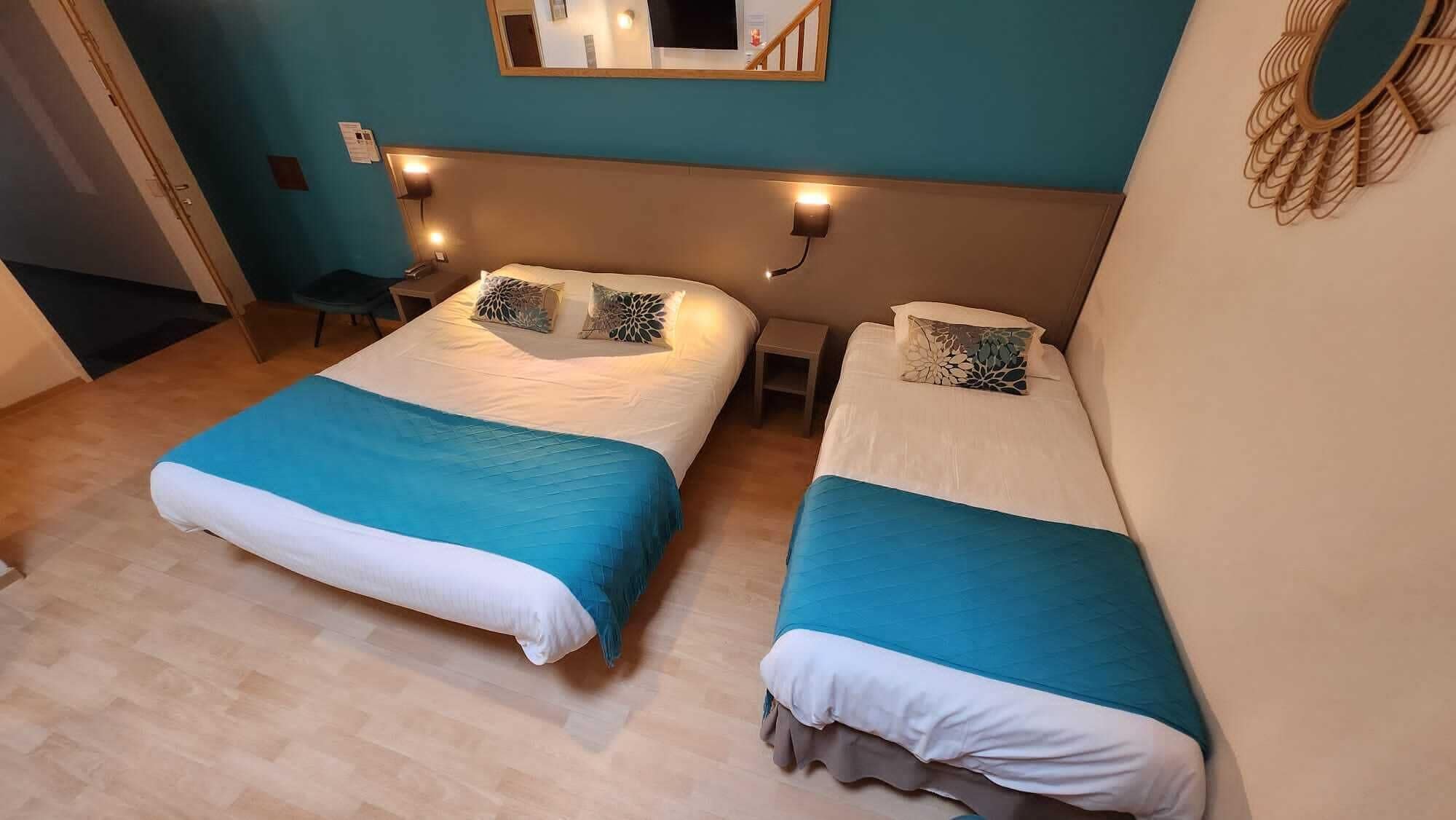 Habitación con dos camas, cada una con una colcha azul y blanca, una mesita de noche pequeña, un espejo montado en la pared y una lámpara sobre el espejo.