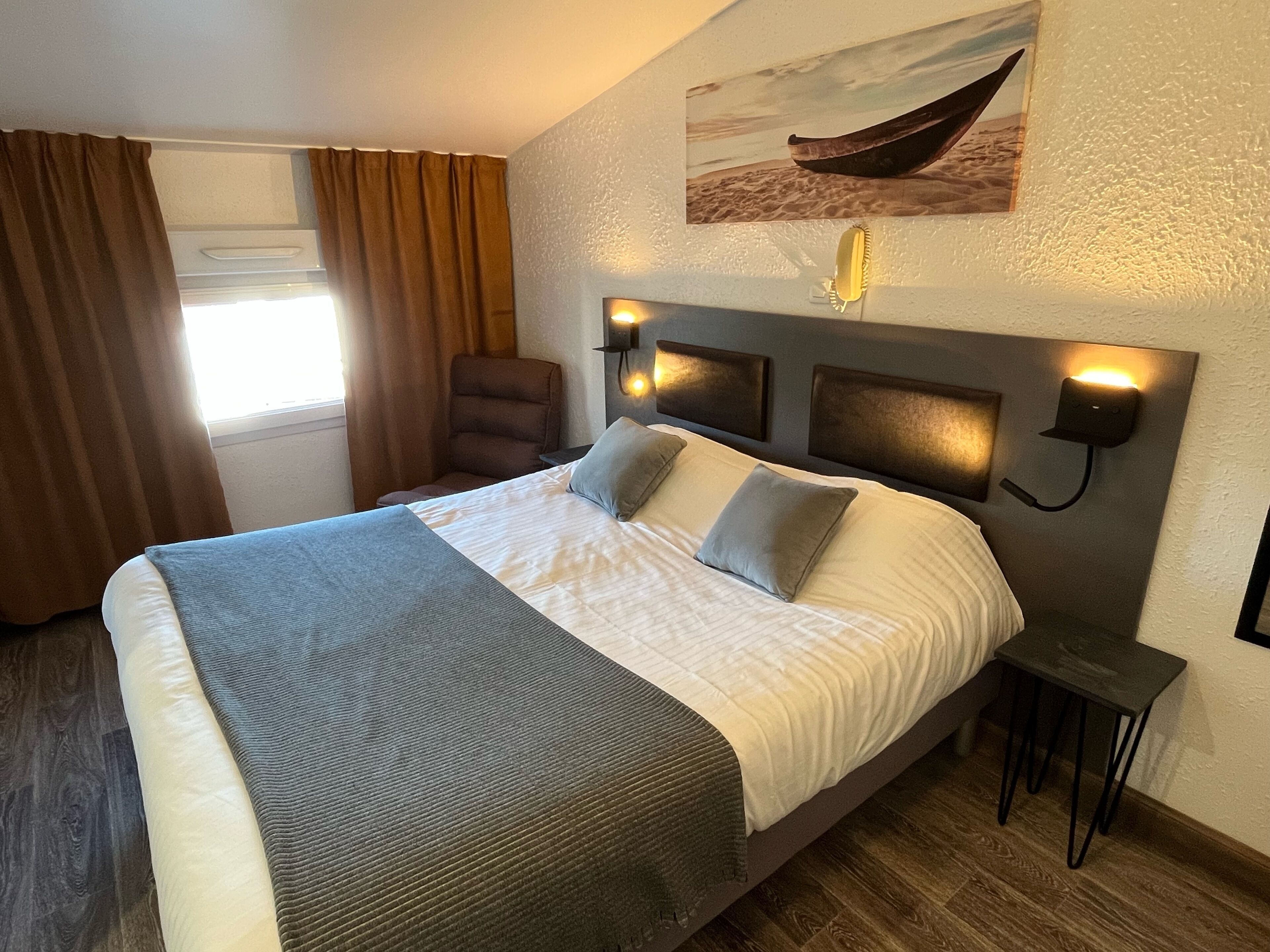 Une chambre d’hôtel avec un grand lit, une chaise, une table de chevet et une lampe fixée au mur.
