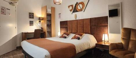 A hotel room with a large bed, bedside tables, a desk, a chair, a TV, and a wall-mounted artwork.