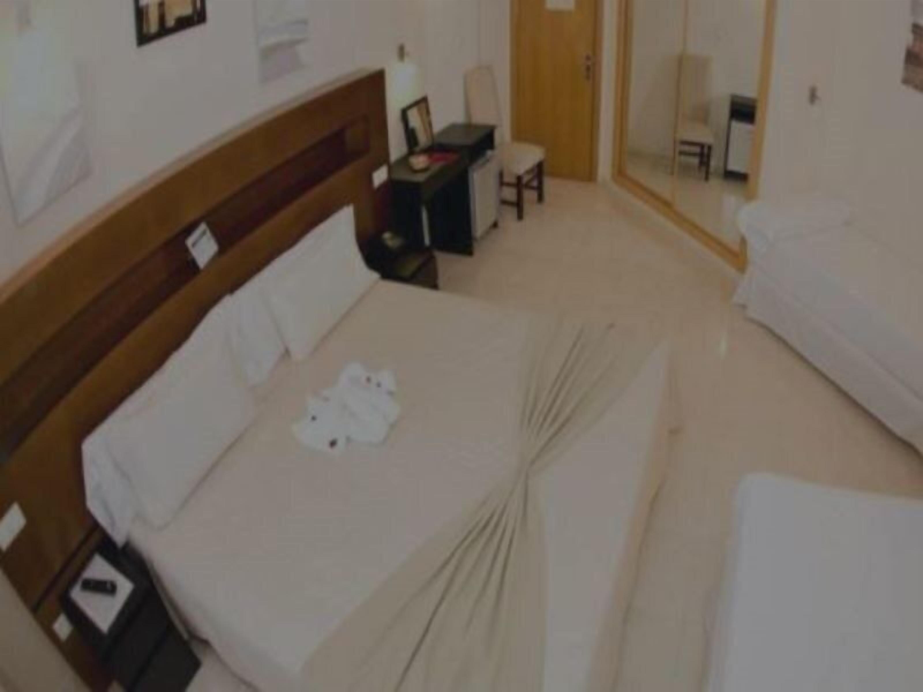 A hotel room with a bed, a desk, a chair, and a mirror.