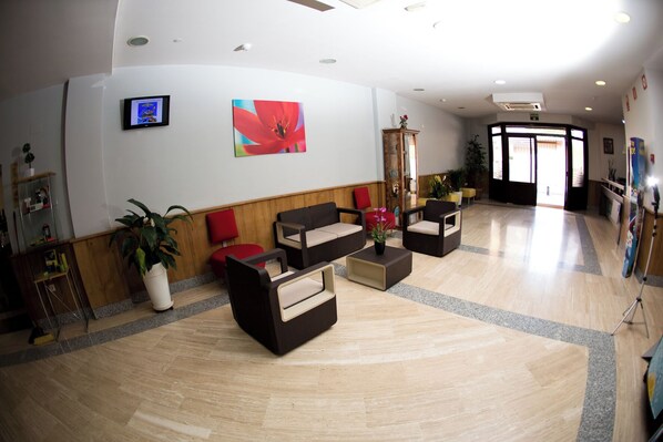 A spacious lobby with a wooden floor, a large red flower painting, and a television mounted on the wall. - Hostal San Marcos (San Martin de la Vega)