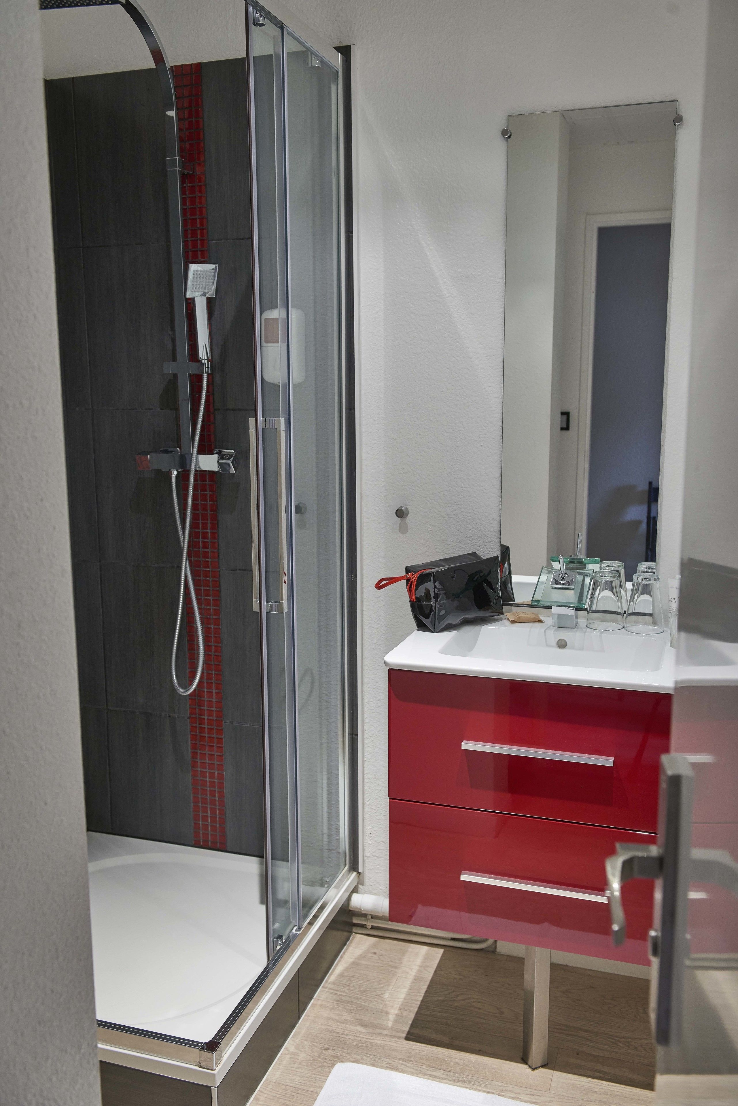 A modern bathroom with a glass-enclosed shower, a white sink, and a red vanity.