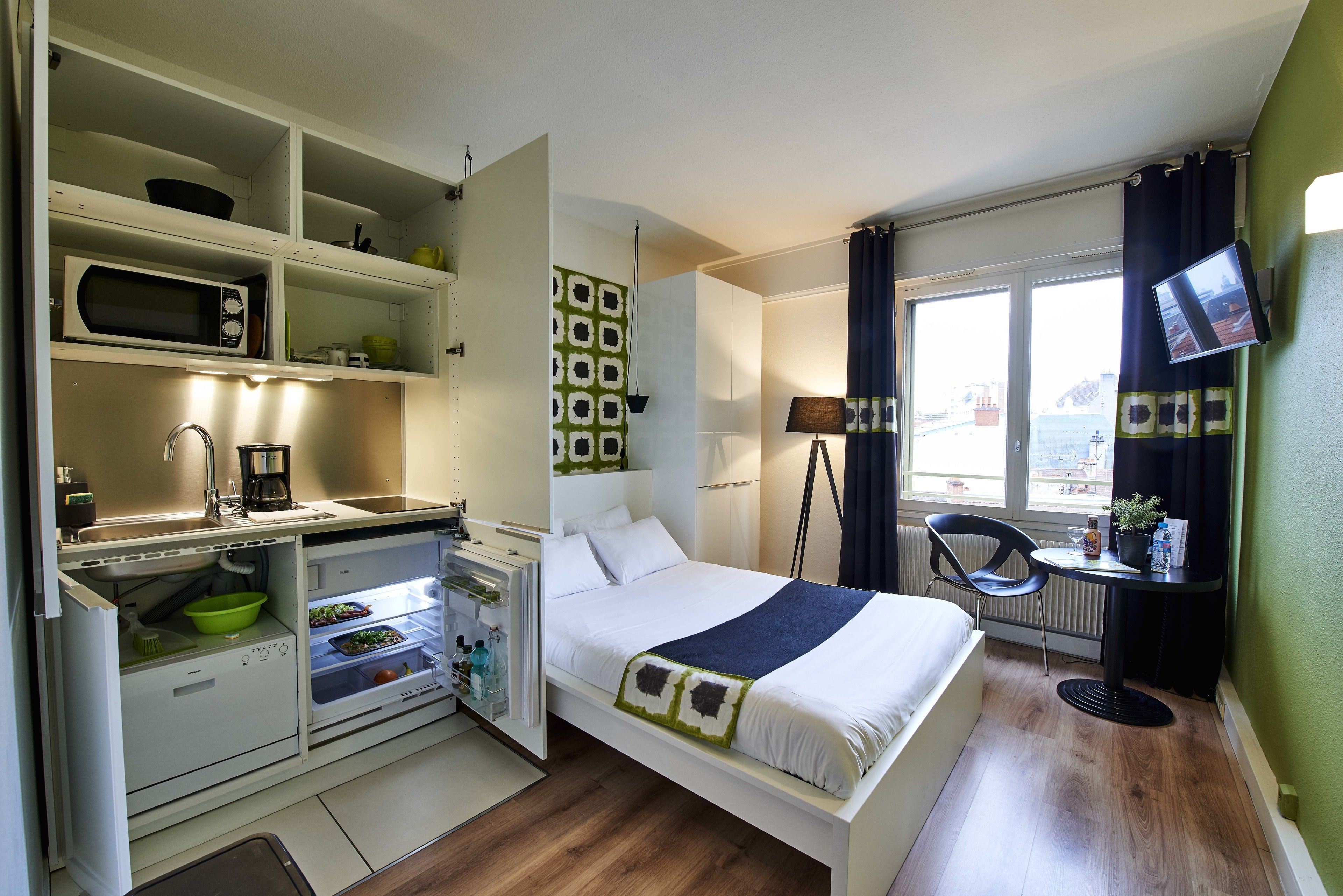Een compacte hotelkamer met een kitchenette, een bed, een klein tafeltje en een televisie.