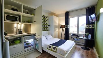 Een compacte hotelkamer met een kitchenette, een bed, een klein tafeltje en een televisie.