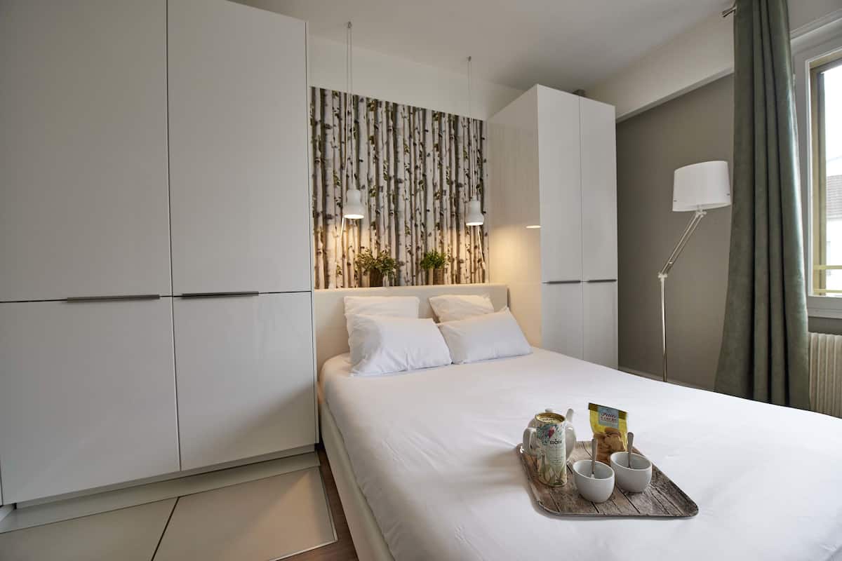 A modern bedroom with a large bed, white bedding, a wall-mounted plant, and a tray with breakfast items.