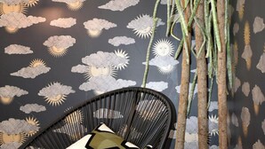 A room with a black chair, a round wooden table, and a wall with a weather-themed wallpaper. - L'aparthoteL LhL (Dijon)