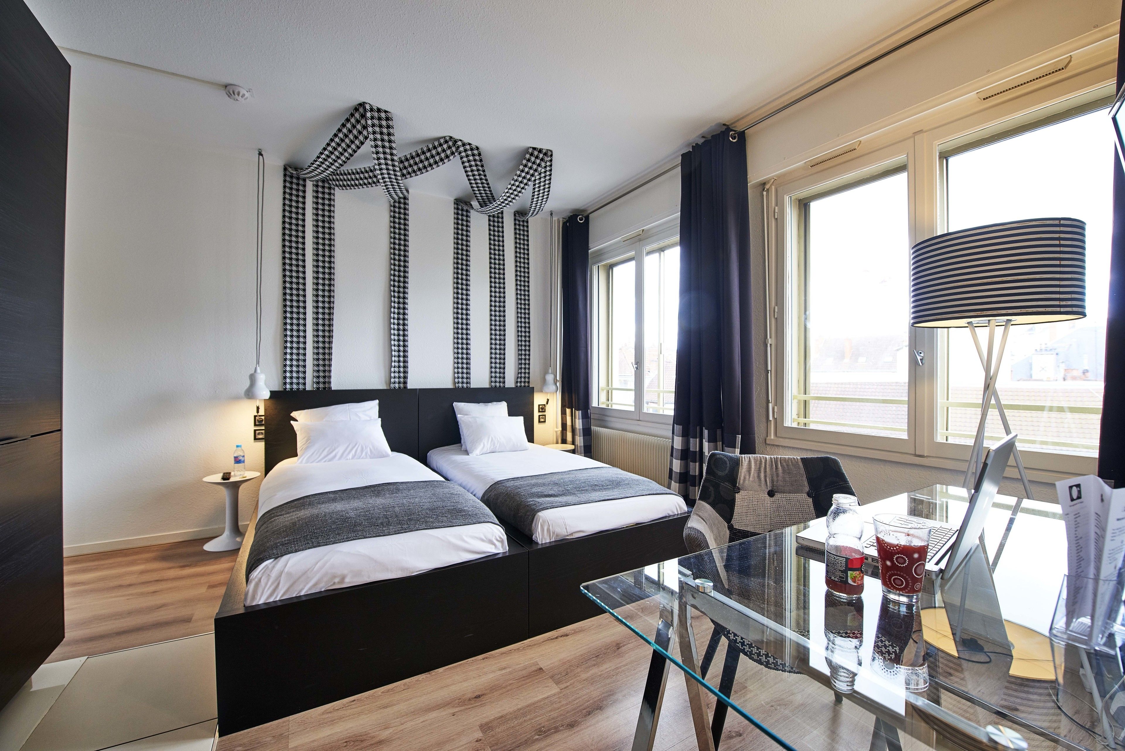Ein modernes Hotelzimmer mit einem großen Bett, einem Glastisch und Blick auf die Stadt durch große Fenster.