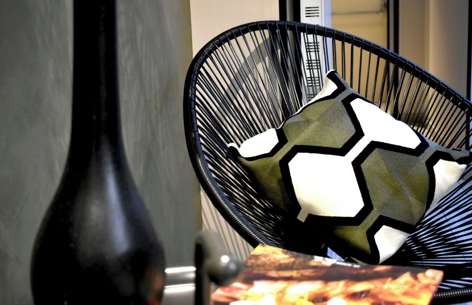 A black chair with a geometric patterned cushion, a black vase, and a poster with a fiery image.
