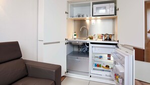 A compact living space with a kitchenette, a brown sofa, and a small plant. - L'aparthoteL LhL (Dijon)