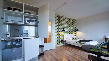 Een compacte hotelkamer met een kitchenette, een bed tegen een muur met patroon en een zithoek.