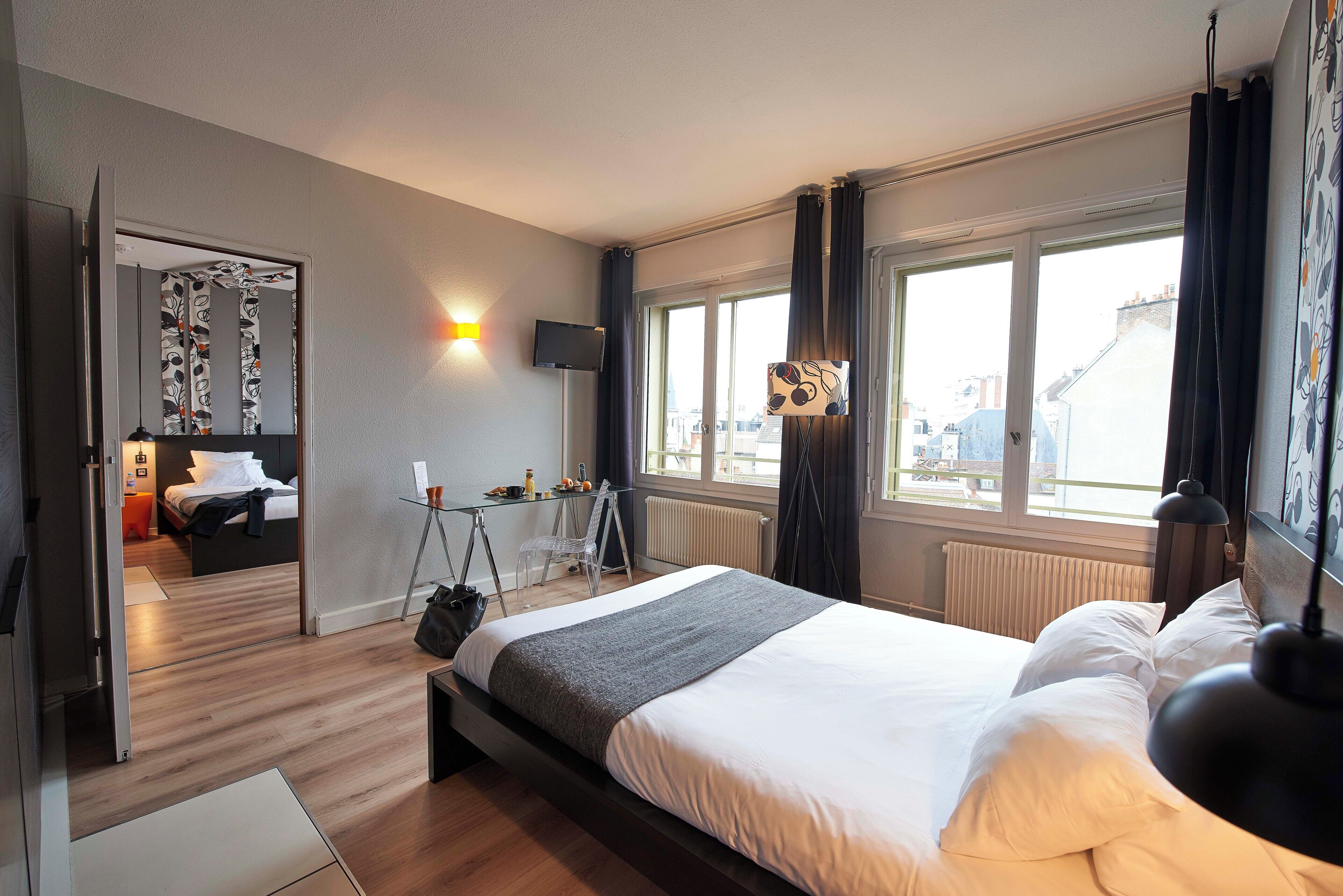 Ett modernt hotellrum med en stor säng, ett skrivbord med en stol, en TV och ett fönster med gardiner.