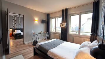 Ett modernt hotellrum med en stor säng, ett skrivbord med en stol, en TV och ett fönster med gardiner.