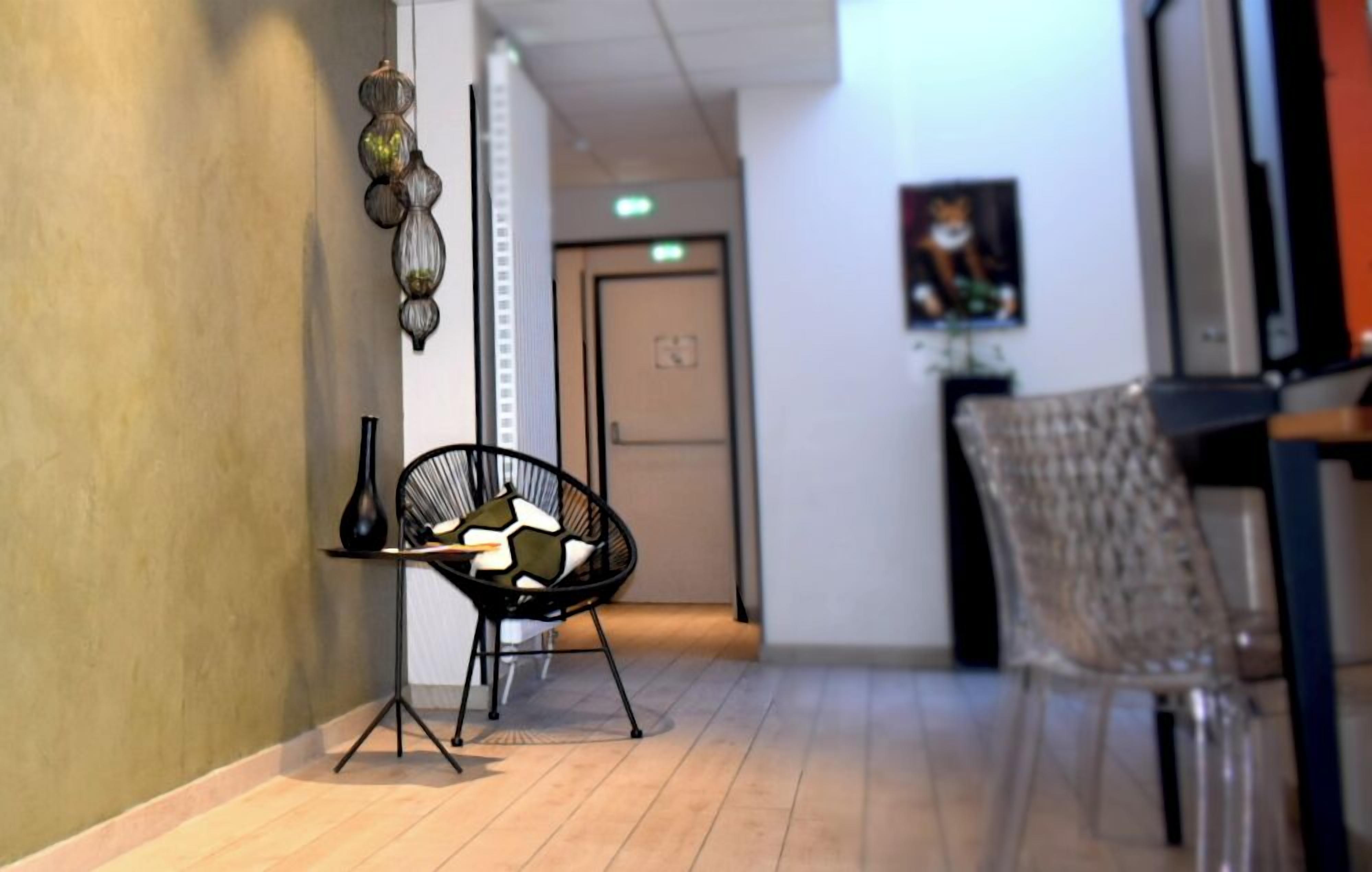 A hallway with a clear view of a door, a chair, and a table with a vase and a pillow.