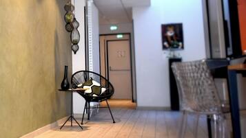 A hallway with a clear view of a door, a chair, and a table with a vase and a pillow.