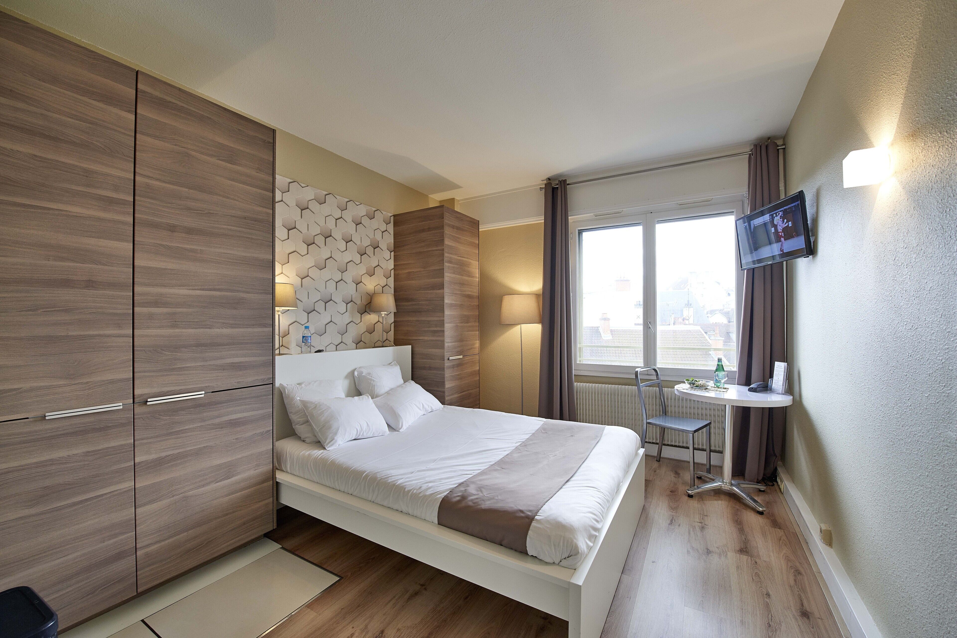 A modern hotel room with a bed, a desk, and a TV.