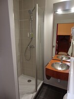 Un baño con ducha envuelta en vidrio, tocador de madera con dos lavamanos y un espejo sobre el tocador.