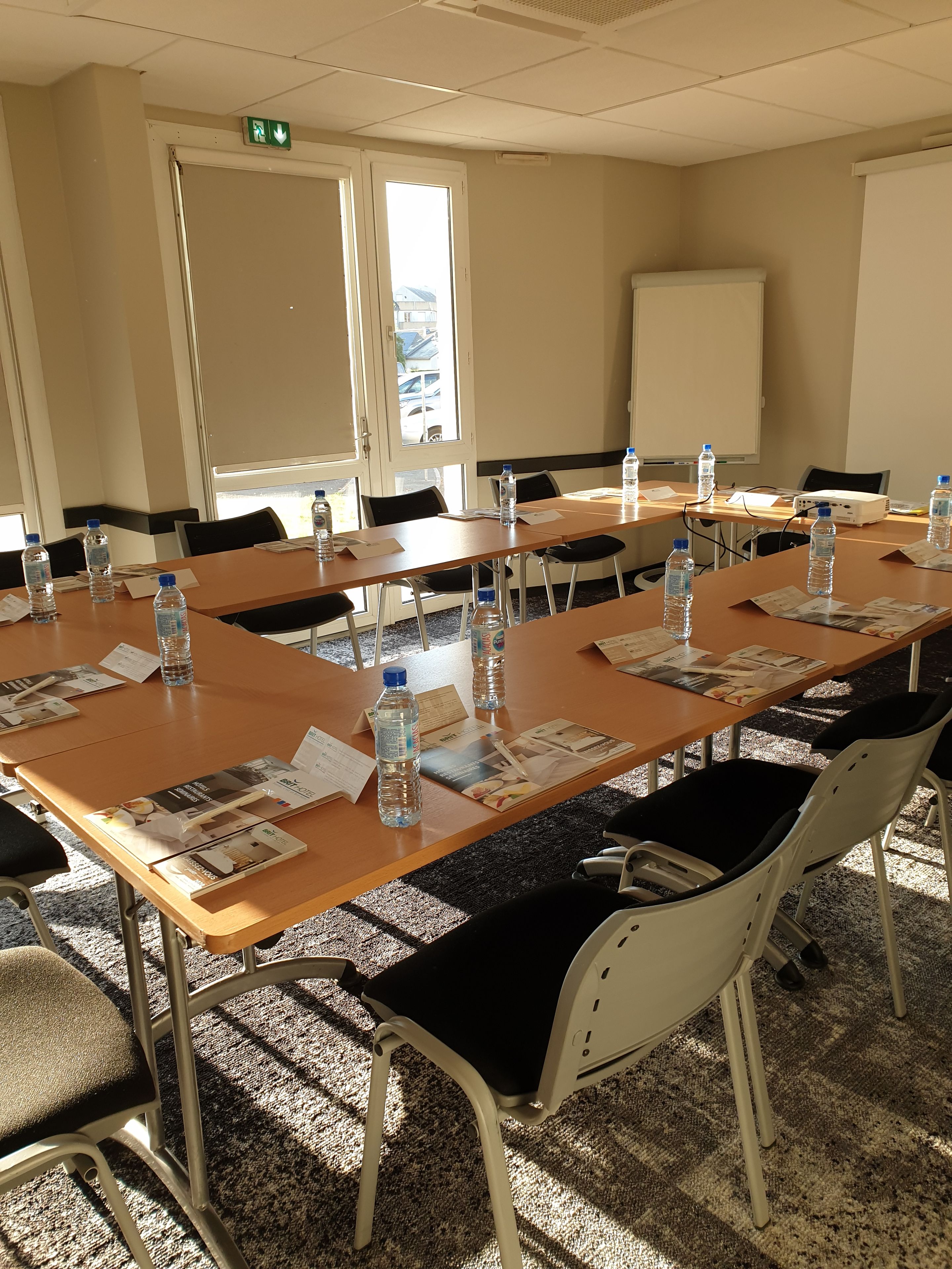 Une salle de conférence équipée de tables, de chaises, de bouteilles d’eau et de documents.