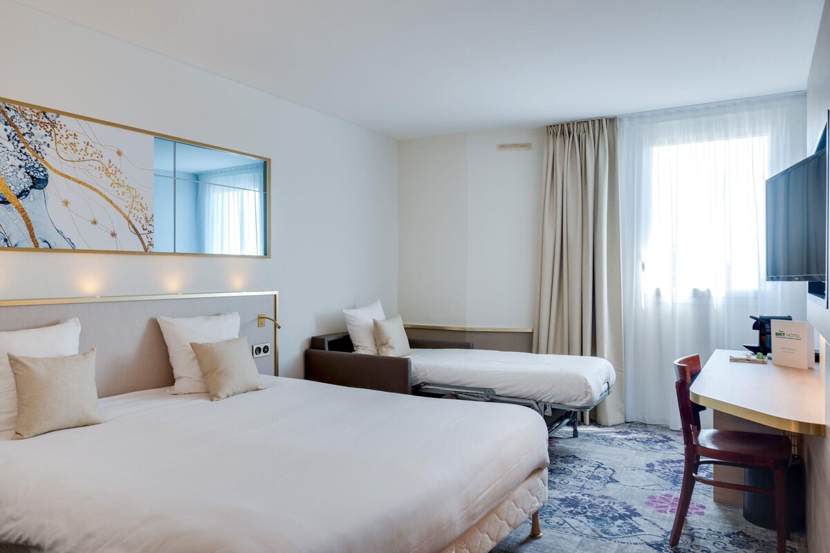 Ein Hotelzimmer mit zwei Betten, einem Schreibtisch, einem Stuhl, einem großen Spiegel und einem Fenster mit Vorhängen.