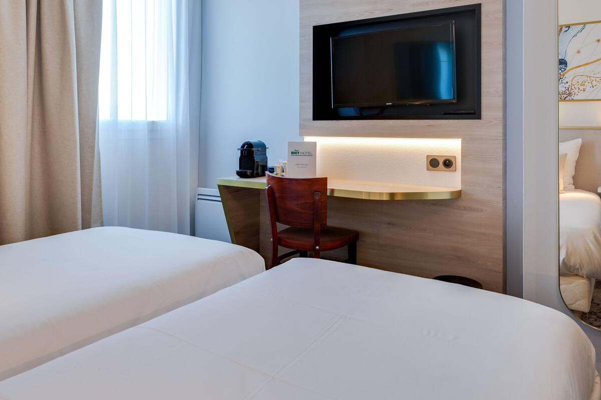 Une chambre d’hôtel avec deux lits, un bureau avec une machine à café, un téléviseur fixé au-dessus du bureau et un miroir au mur.