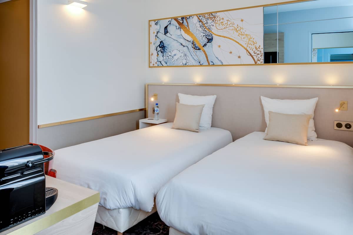 Une chambre d’hôtel avec deux lits, un minibar, une machine à café et un grand tableau abstrait accroché au mur.