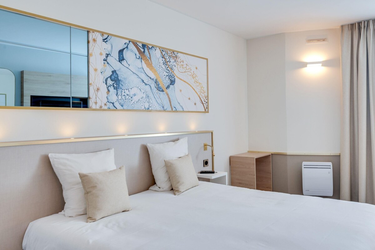 Ein Hotelzimmer mit einem großen Bett, einem Nachttisch, einer Wand-Klimaanlage und einem großen, abstrakten Gemälde über dem Bett.