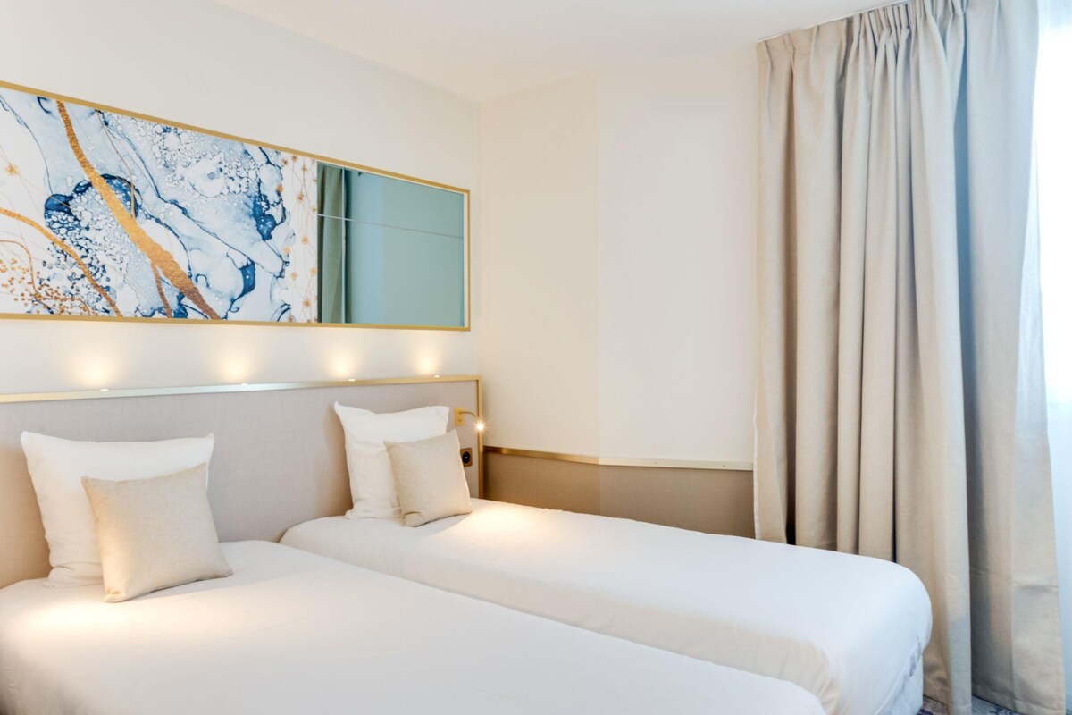Ein Hotelzimmer mit zwei Betten, einem großen Spiegel und Meerblick aus dem Fenster.