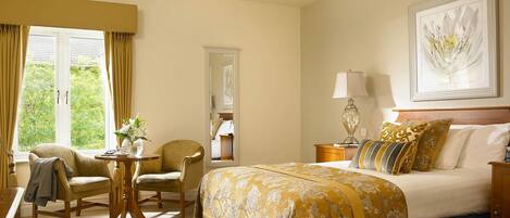 A hotel room with a bed, a desk, a chair, a lamp, and a painting on the wall.