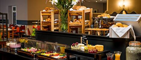 A buffet with various food items, a vase of flowers, and a sign indicating available cheese and other options.